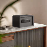 A matte black electronic safe with a digital keypad, displayed on a marble-topped cabinet in a modern home interior setting.