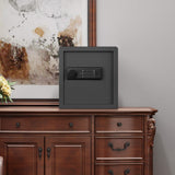 A black safe with a keypad and remote control, displayed on a brown wooden cabinet in front of a framed abstract painting.